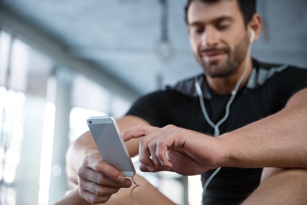 Portrait of a fitness man using smartphone in gym. Focus on smartphone.jpg