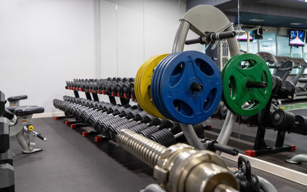 Colour-coded bumper plates and barbell on a rack in a strength training area of a gym.