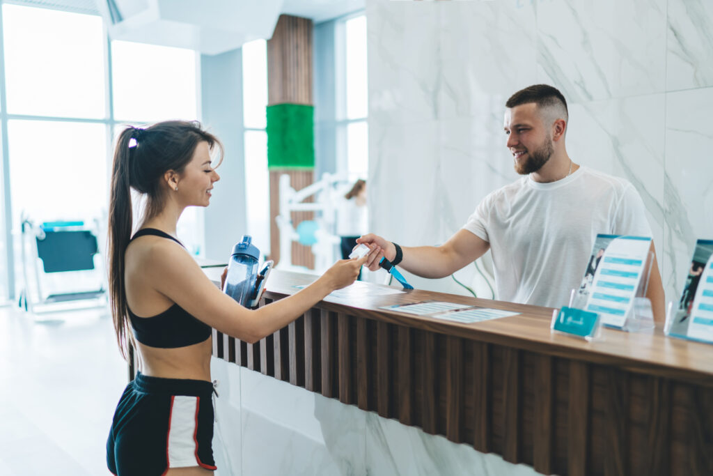 Gym member checking in at reception using a wristband scanner in a modern, bright facility.