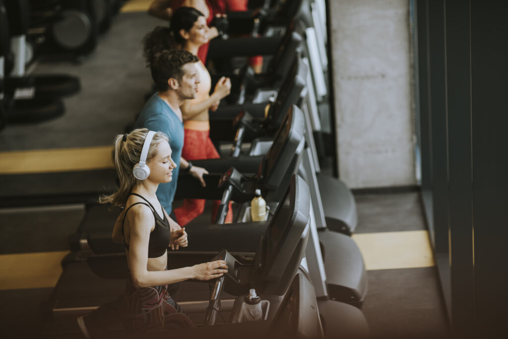 Group of adults running on treadmills in a modern gym with natural lighting, showcasing an active fitness community and professional workout environment.