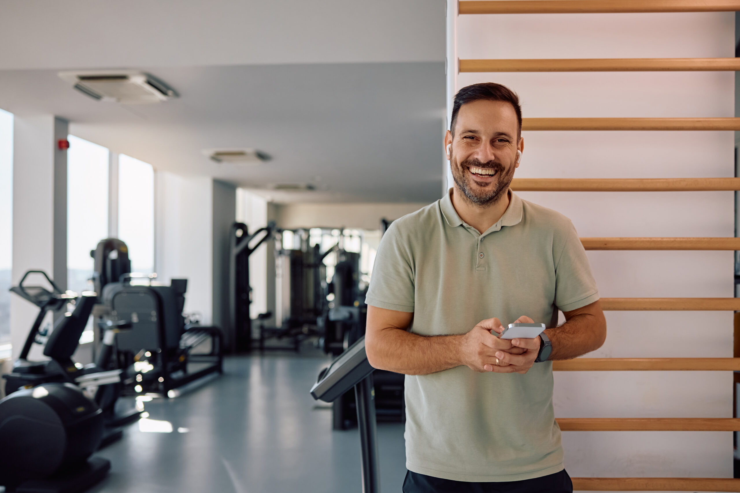Happy athlete using smart phone in fitness center and looking at camera.