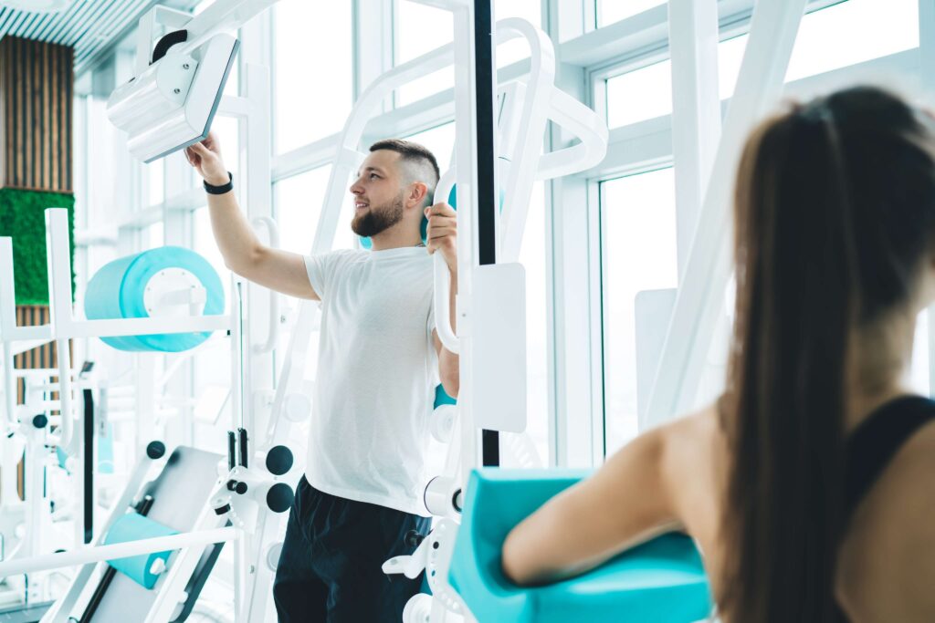 Man adjusting fitness machine settings in a bright modern gym.