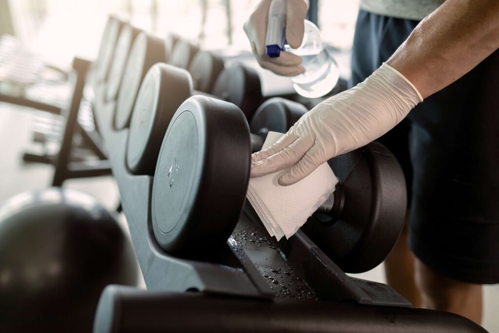 Person wearing gloves cleaning dumbbells with spray and paper towel.