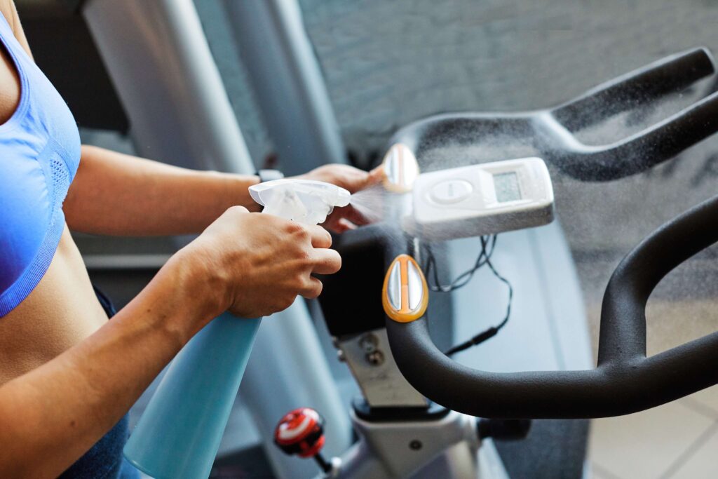 Woman spraying disinfectant on exercise bike handlebars at the gym.