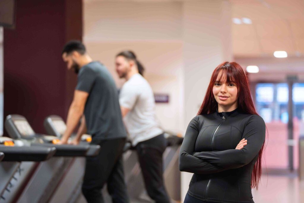 Gym trainer standing confidently in a modern fitness studio, representing strong gym branding and professional image.